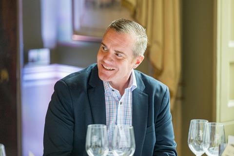 Photograph of Carpenters Group director of claims strategy Simon Smith smiling while engaging in conversation. He wears a blue and yellow chequered shirt and navy blazer.